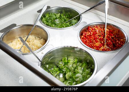 Vista su un banco di condimenti, con contenitori per aglio, scallio, peperoncino rosso e coriandolo, visti in un ristorante locale. Foto Stock