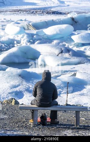 Un fotografo che fotografa gli iceberg galleggianti nella laguna del ghiacciaio Jokulsarlon in Islanda. Indossa una giacca nera invernale Foto Stock