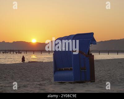 Una sola sdraio sulla spiaggia al tramonto, persone e molo sullo sfondo, binz, ruegen, Mar baltico, germania Foto Stock