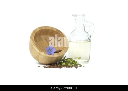 Mortaio di legno riempito con piccoli semi di lino marrone e fiori di pianta di lino blu insieme all'olio di lino in decanter di vetro isolato su fondo bianco Foto Stock