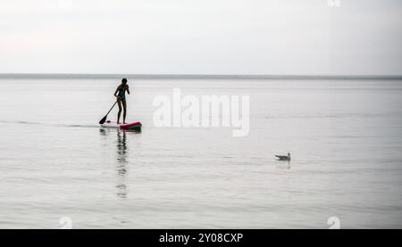 Una ragazza su un paddleboard soffia le placide acque del lago Huron. Foto Stock