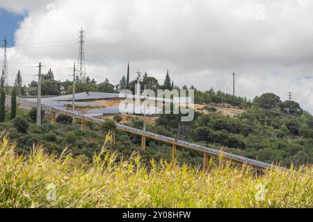 Nastro trasportatore che trasporta pannelli solari fotovoltaici per l'installazione su una collina, simboleggiando la transizione verso fonti di energia rinnovabili Foto Stock