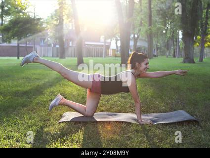 Donna che si allunga in un esercizio all'aperto sorridente felice facendo stretching dopo la corsa. Splendido modello sportivo sorridente all'aperto al tramonto d'estate Foto Stock