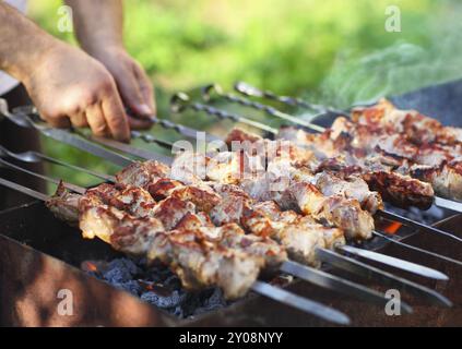 Uomo di cottura spiedini marinati, carne di agnello grigliare su spiedino di metallo, close up Foto Stock