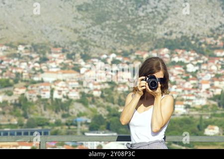 Donna che scatta una foto da un punto di vista, tenendo una fotocamera DSLR al volto. Ritratto di una fotografa che guarda attraverso il mirino di una fotocamera Foto Stock