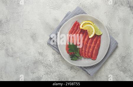 Salmone salmone, affumicato a freddo, tagliato a fette, su un piatto grigio, con limone e prezzemolo, vista dall'alto, primo piano, nessuno Foto Stock