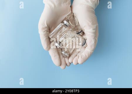 Trattamento medico, concetto di vaccinazione. Il medico le mani in guanti bianchi che tengono le bottiglie con il vaccino, l'antibiotico o altri medicamenti su sfondo blu Foto Stock