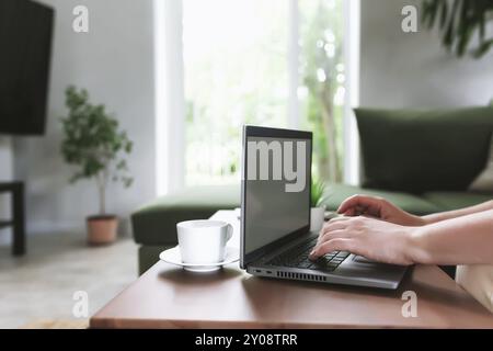 Digitazione a mani, stampa su notebook grigio. Lavoro da casa, spazio di lavoro, scrivania, concetto di lavoro remoto, schermo vuoto vuoto su tavolo di legno con bianco Foto Stock