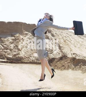 Felice donna d'affari che salta in aria in un deserto Foto Stock