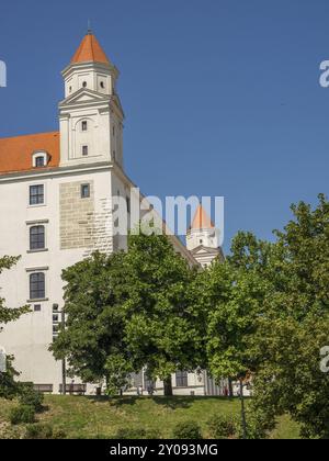 Vista laterale di un castello con torri e tetto arancione, circondato da alberi, bratislava, slovacchia Foto Stock