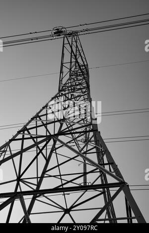 Primo piano bianco e nero di una torreggiante struttura di linee elettriche contro un cielo limpido e senza nuvole. Foto Stock