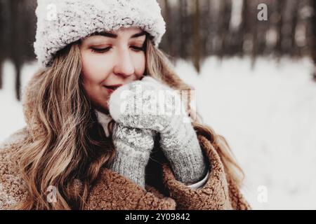 Bella giovane donna in neve fantasia bosco invernale. Ragazza che indossa morbidi guanti, cappuccio e cappotto. Foresta di Natale, alberi su sfondo sfocato. Incrociato Foto Stock