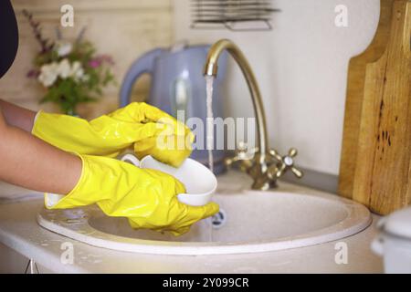 Chiudere fino a mani della donna che indossa guanti gialli lavaggio piatti nella cucina. Procedimento per il lavaggio di stoviglie Foto Stock