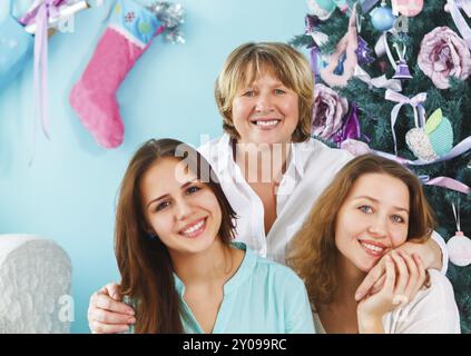 Primo piano ritratto di una madre matura e di una figlia adulta e di una nipote adolescente che si avvicinano e si abbracciano a casa vicino all'albero di Natale che sono felici e.. Foto Stock