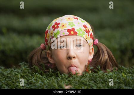 La bambina si nasconde tra le siepi e si sporge la lingua Foto Stock