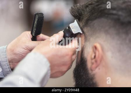 Bell'uomo barbuto, che viene tagliato dal barbiere, con rifinitore elettrico al barbiere Foto Stock