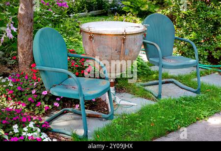 Arredi esterni da patio con sedie in metallo verde e un vecchio tamburo timpani riutilizzato (kettledrum) utilizzato per un tavolo finale. Foto Stock