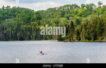 Una persona che pagaia in kayak sul lago Mink, nella contea di Cook nel Minnesota settentrionale, con la Superior National Forest sullo sfondo. Foto Stock