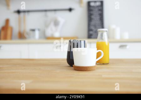 Tavolo in legno con mug, bricco per il latte e il succo d'arancia con cucina sfocata sfondo, spazio di copia Foto Stock