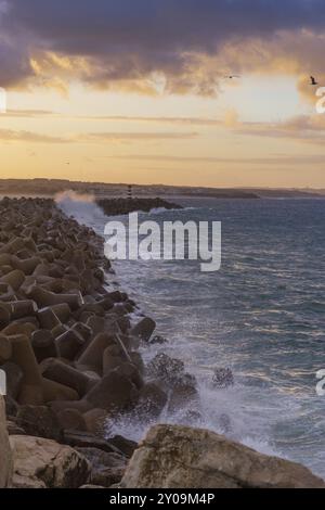 Faro di Peniche con spiaggia di Supertubos sullo sfondo al tramonto con onde che si infrangono, in Portogallo Foto Stock