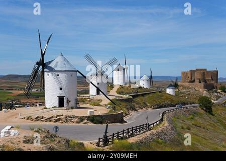 Diversi mulini a vento bianchi su una collina, con un castello sullo sfondo sotto un cielo blu, Consuegra, Toledo, Castilla-la Mancha, percorso di Don Chisciotte, Spai Foto Stock