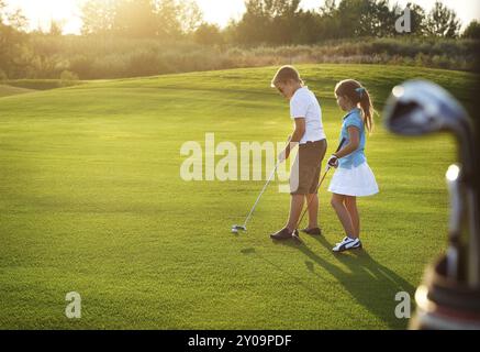 Casual i bambini in un campo da golf holding club di golf. Tramonto Foto Stock