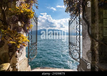 Porta di ferro ornata di Villa Cipressi a Varenna che apre su una vista panoramica del Lago di Como in una giornata di sole, Italia Foto Stock