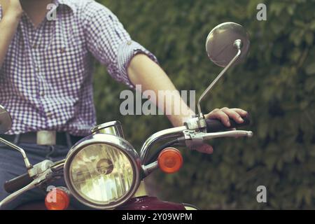 Giovane uomo che cavalca il vecchio scooter retrò in una strada di città Foto Stock