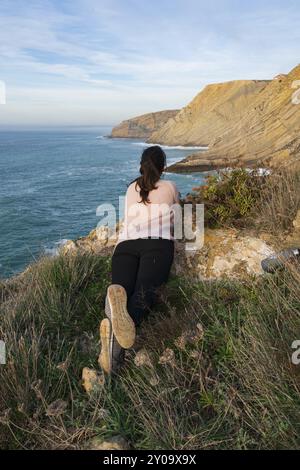 Donna su una camicia rosa che guarda il paesaggio di Cabo Espichel Capo mare scogliere e l'oceano atlantico, in Portogallo Foto Stock