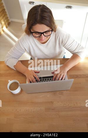 Vista dall'alto di womans mani digitando sulla tastiera del notebook con gli occhiali e il caffè sul tavolo. Mock up minimo piatto eroe laico la testata Foto Stock