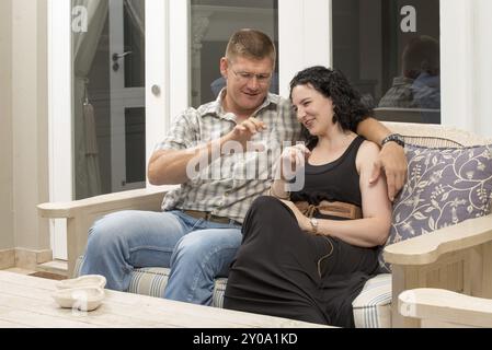 Una giovane coppia adulta seduta insieme su un divano nel patio, comunicando tra loro in modo rilassato Foto Stock