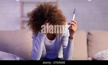 Ragazza depressa che tiene il test di gravidanza coprendo il viso con la mano Foto Stock