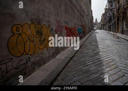 Catania, Italia - 18 maggio 2024: Via vuota con graffiti sul muro. Chiesa di San Nicolo sullo sfondo. Foto Stock