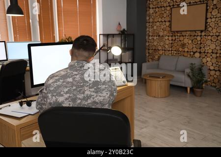 Giovane soldato maschio che lavora con il computer mentre parla al telefono nel quartier generale, vista posteriore Foto Stock