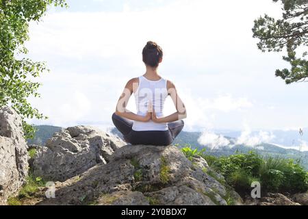 Attraente giovane donna facendo un po' di yoga posa per il saldo sulla cima della roccia alta in montagna giornata soleggiata cielo blu con nuvole Foto Stock