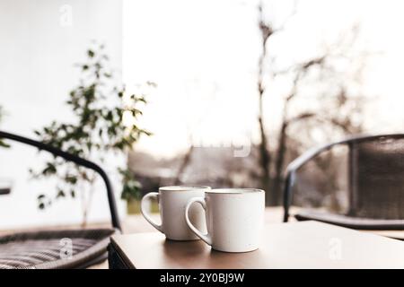 Due tazze di caffè sul tavolo sulla terrazza di legno marrone durante il tramonto serale con sfondo sfocato. Relax, concetto di caffetteria o ristorante Foto Stock