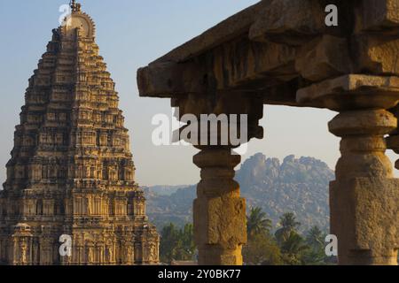 Le colline che circondano le antiche rovine di Hampi sono viste attraverso le colonne scolpite e il vicino tempio Virupaksha a Karnataka, India, Asia Foto Stock