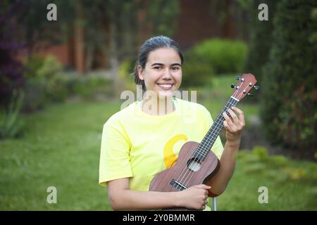 Carino teen ragazza che gioca il suo ukulele all'aperto di sera Foto Stock