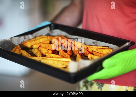 Immagine ravvicinata di patate arrosto e pastinaca in un vassoio. Un uomo è in azienda è nelle sue mani indossando i guanti da forno. Tempo di festa Foto Stock