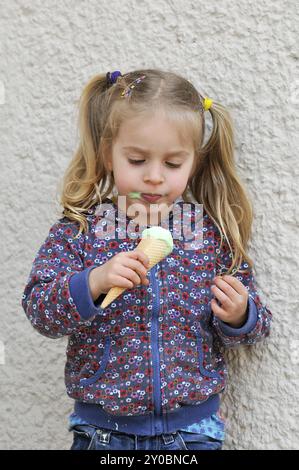 Una bambina carina con capelli biondi e pigtail che mangia un cono gelato. Una bambina carina con capelli biondi e pigtail che mangia gelato Foto Stock