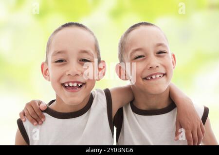 Due gemelli sorridenti e felici si abbracciano l'un l'altro sullo sfondo verde primaverile Foto Stock