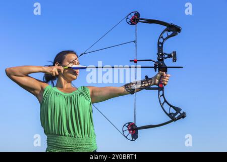 Giovane nero capelli donna colombiano freccia di puntamento di arco composto nel cielo blu Foto Stock