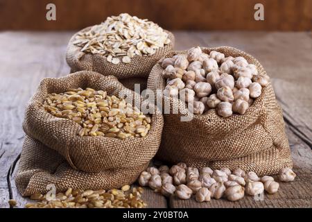 Cereali per una dieta sana, frumento, farina d'avena e ceci in sacchi su fondo rustico in legno Foto Stock