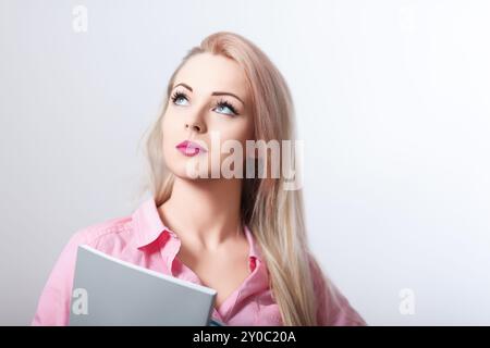 La giovane donna è profondamente pensata mentre tiene un libro, forse sta cercando ispirazione o sta cercando di ricordare qualcosa Foto Stock