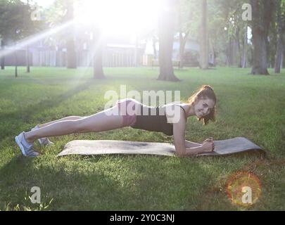 Donna che si allunga in un esercizio all'aperto sorridente felice facendo stretching dopo la corsa. Splendido modello sportivo sorridente all'aperto al tramonto d'estate Foto Stock