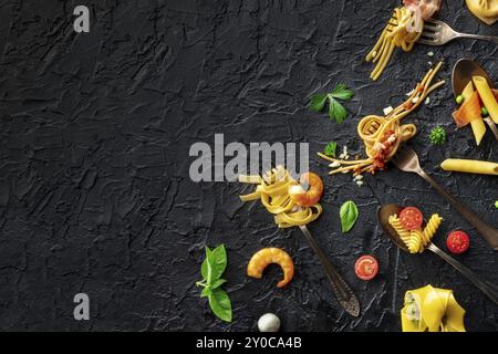 Varie forchette per la pasta. Spaghetti, fusilli, penne e altre forme di pasta, con salsa, scattati dall'alto su uno sfondo di ardesia nera con spazio per la copia Foto Stock