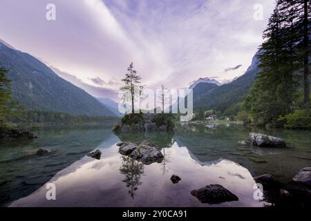 Hintersee con rocce e alberi in primo piano, circondato da montagne dopo il tramonto con un cielo nuvoloso, Ramsau, il Parco Nazionale di Berchtesgaden, Foto Stock