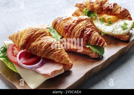 Varietà di panini con croissant. Vari croissant ripieni su un tagliere in legno. Panini ripieni di prosciutto, salmone, uovo, fotografia di cibo, fotograp Foto Stock