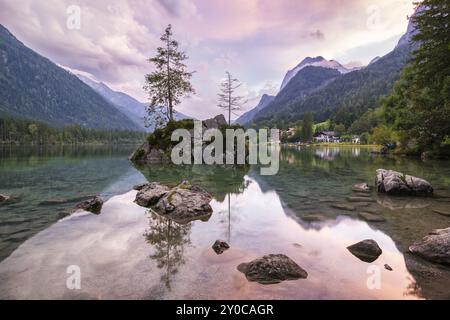 Hintersee con rocce e alberi in primo piano, circondato da montagne dopo il tramonto con un cielo nuvoloso, Ramsau, il Parco Nazionale di Berchtesgaden, Foto Stock