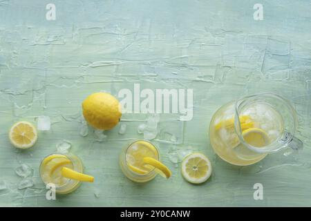 Limonata. Bere acqua di limone con ghiaccio. Due bicchieri e una caraffa su sfondo blu, scattati dall'alto con un posto per il testo. Disintossicazione delle bevande. Fresco h Foto Stock